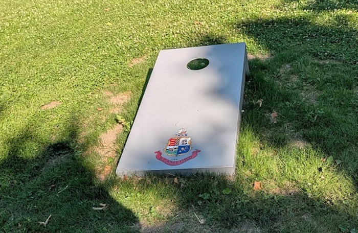 Close-up of a gray cornhole board with a colorful crest displayed near the lower end.
