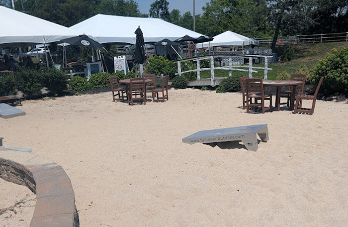 Weatherproof cornhole boards installed in a sandy outdoor recreation area with tables and event tents.
