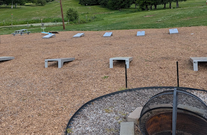 Multiple permanent cornhole boards arranged across a large wood-chip recreation field.